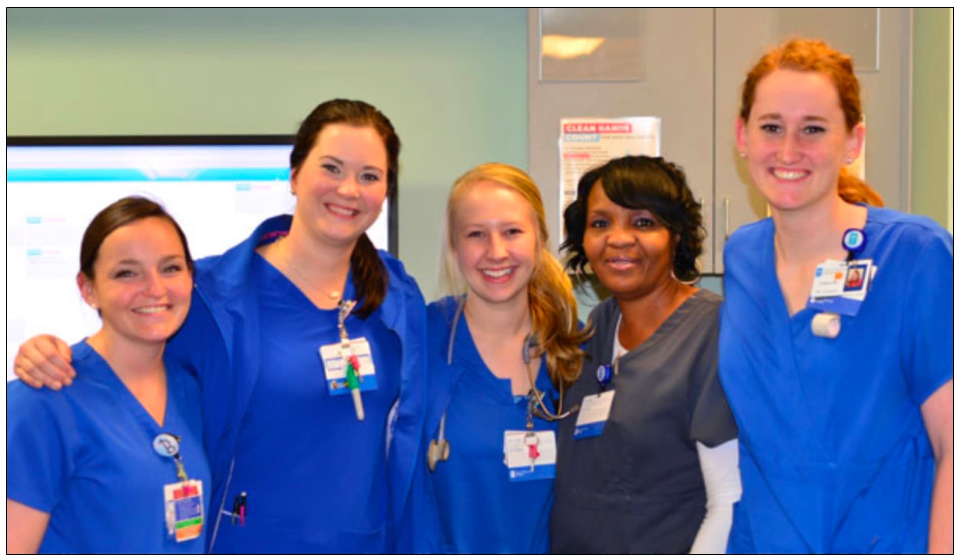 Five nurses in scrubs smiling together on a hospital ward
